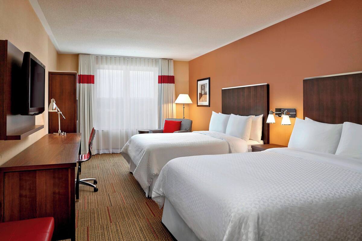 A hotel room with two beds, a desk, a TV, and a window with curtains.