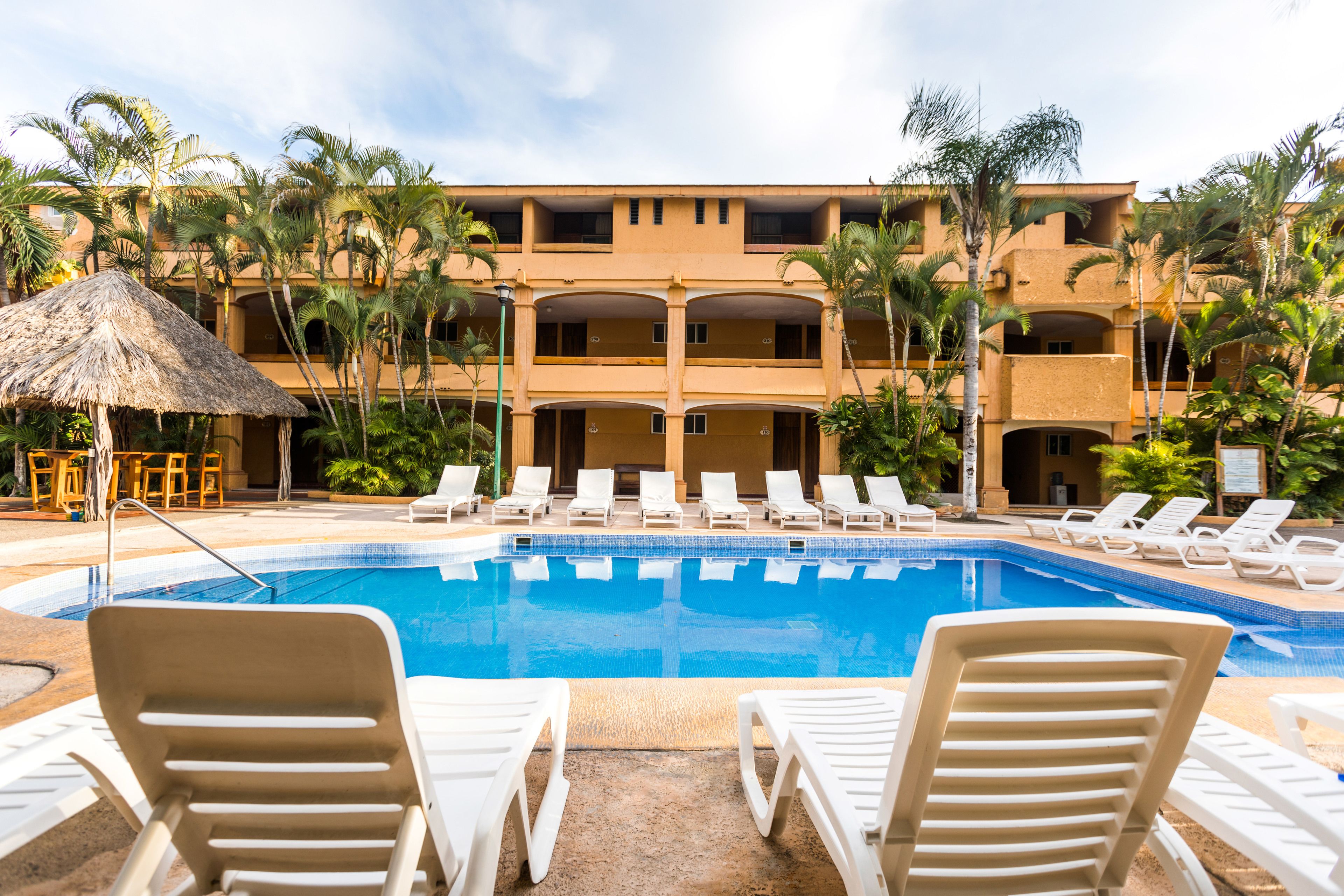 A swimming pool with lounge chairs, palm trees, and a building with multiple balconies.