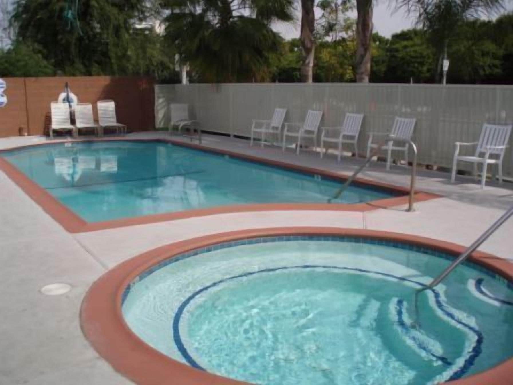 A swimming pool with a hot tub, surrounded by lounge chairs and a fence.