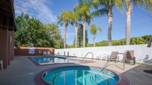 A pool area with two pools, lounge chairs, and palm trees. - Abby's Anaheimer Inn (Anaheim)