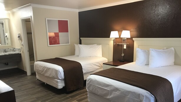 A hotel room with two beds, a bathroom, and a wall-mounted artwork. - Abby's Anaheimer Inn (Anaheim)