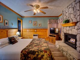 A bedroom with a bed, a television, a fireplace, and a ceiling fan.
