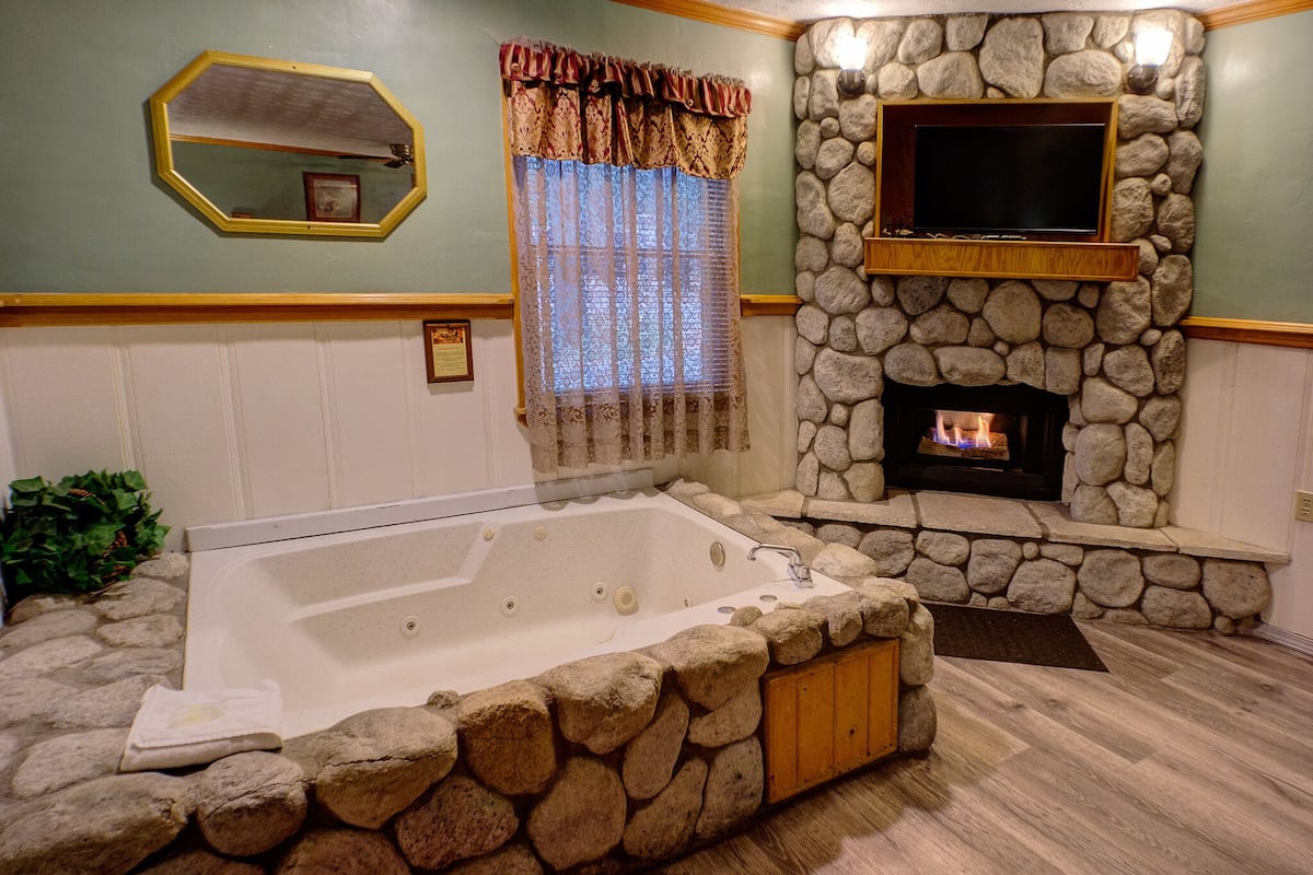 A bathroom with a stone wall, a built-in fireplace, and a large bathtub.
