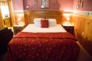 A hotel room with a large bed, wooden headboard, and two bedside tables with lamps.