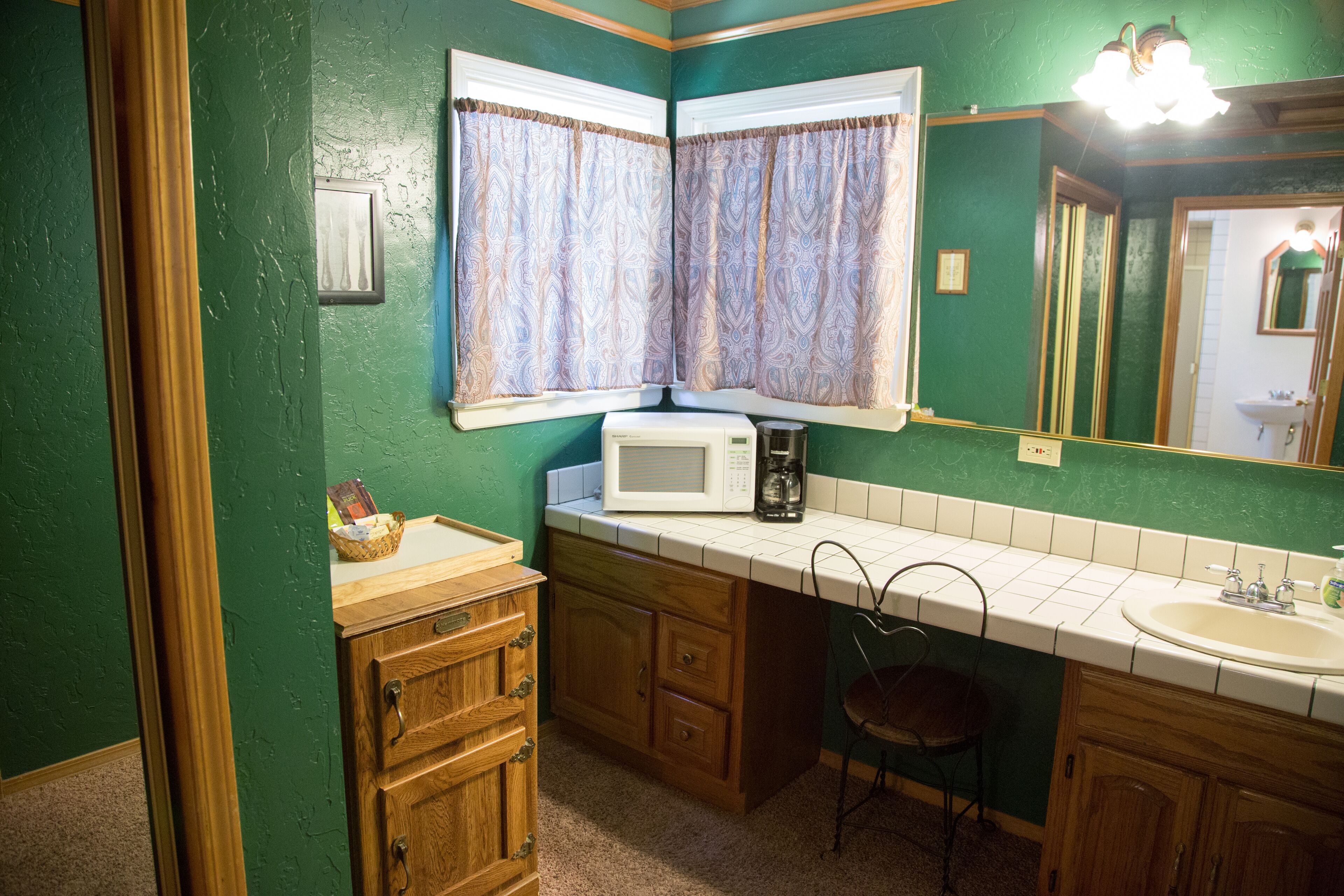 A bathroom with green walls, a wooden vanity, a white sink, a mirror, and a window with patterned curtains.