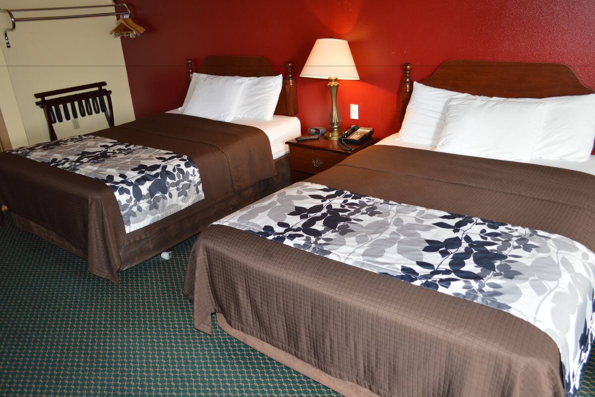 Habitación de hotel con dos camas, una mesita de noche con lámpara, teléfono y perchero.