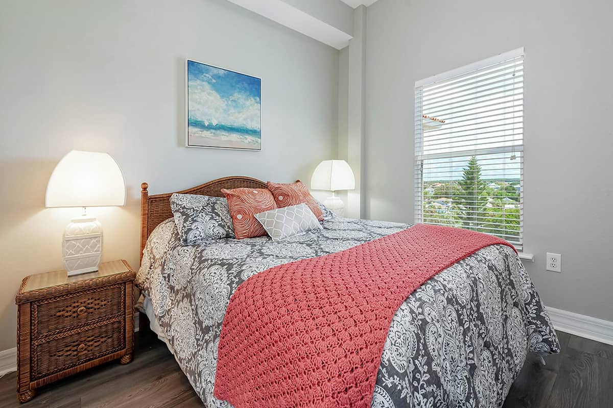 Une chambre à coucher avec un lit, deux tables de chevet avec des lampes, une fenêtre avec des stores et un tableau au mur.