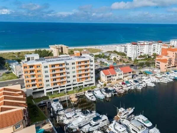 Un port de plaisance où sont amarrés de nombreux bateaux, entouré d’immeubles à plusieurs étages dotés de balcons, à proximité d’une plage.