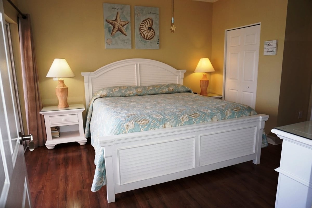 A bedroom with a white bed, two bedside tables with lamps, a door, and two wall decorations.