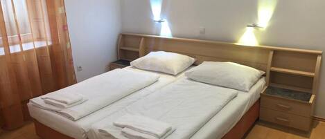 Ein ordentlich bezogenes Bett mit weißen Leinen und Handtüchern, ein hölzernes Kopfteil, ein Nachttisch und ein Beistelltisch.