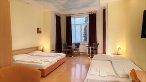 A hotel room with two beds, a small table, chairs, and a window with curtains.