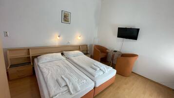 Ein Hotelzimmer mit einem Doppelbett, einem kleinen Tisch, zwei Stühlen, einem an der Wand montierten Fernseher und einem Bild.