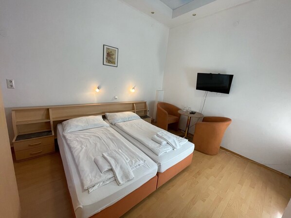A hotel room with a double bed, a small table, two chairs, a TV mounted on the wall, and a picture on the wall.