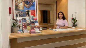 Bancada de recepção com uma mulher em pé atrás dela, cercada por livros e revistas.