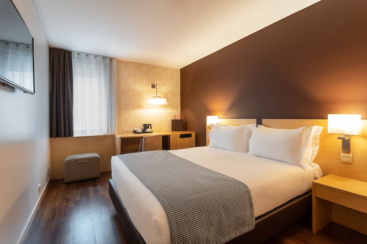 A hotel room with a large bed, bedside tables, a desk, and a chair.