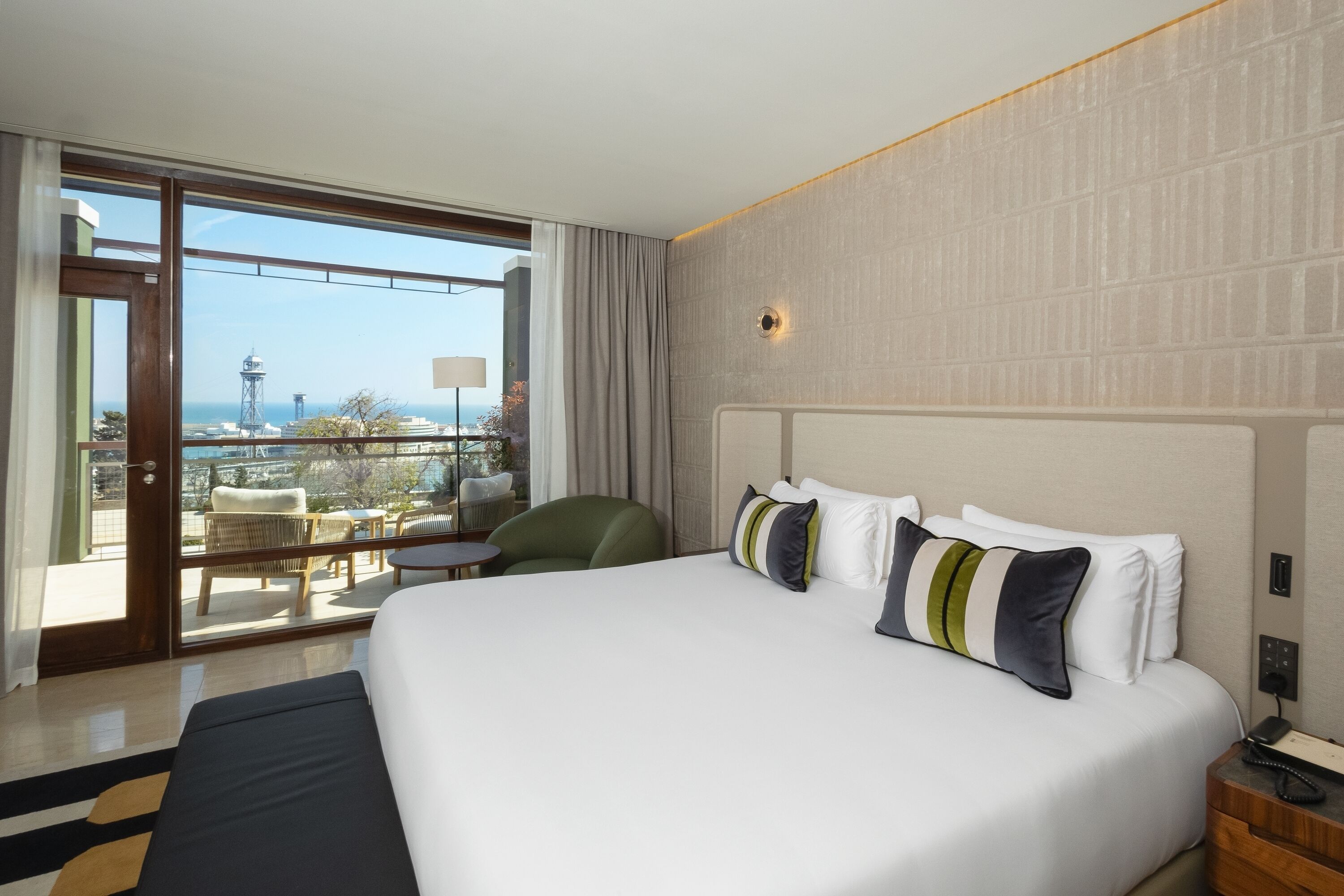 Habitación de hotel con una cama grande, vistas a la ciudad y un balcón con mobiliario exterior.