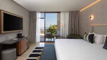 Habitación de hotel con una cama grande, televisión de pantalla plana, escritorio con cafetera, una mesita pequeña y balcón con vistas.
