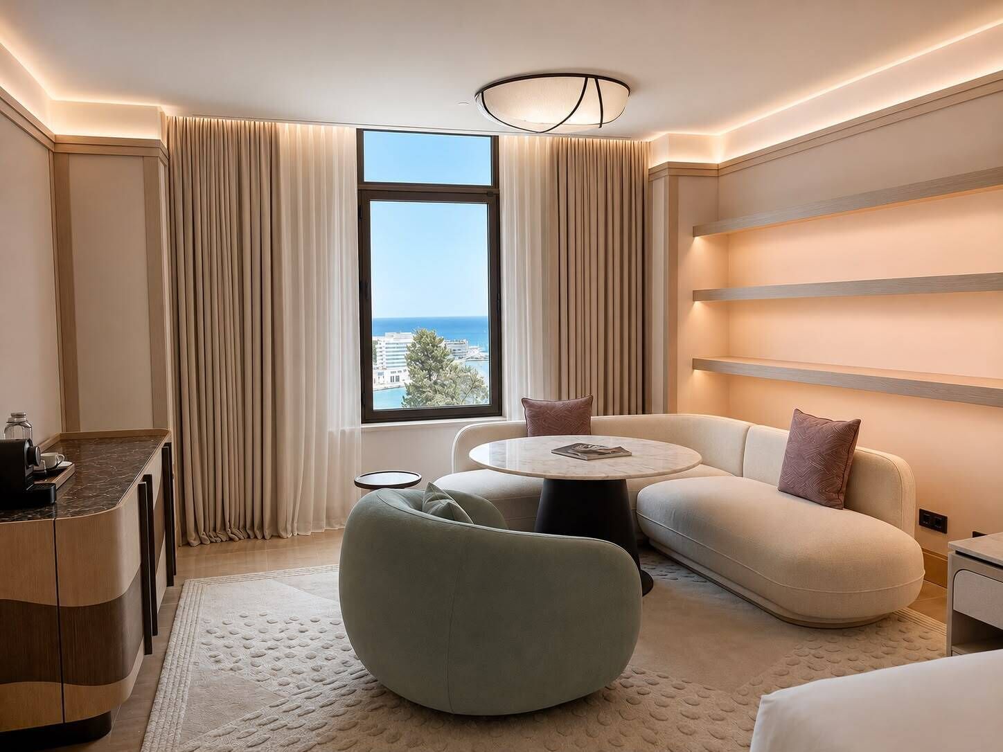 Ein modernes Hotelzimmer mit einer Couch, einem runden Couchtisch, einem kleinen Beistelltisch und einem Schreibtisch mit einer Lampe.