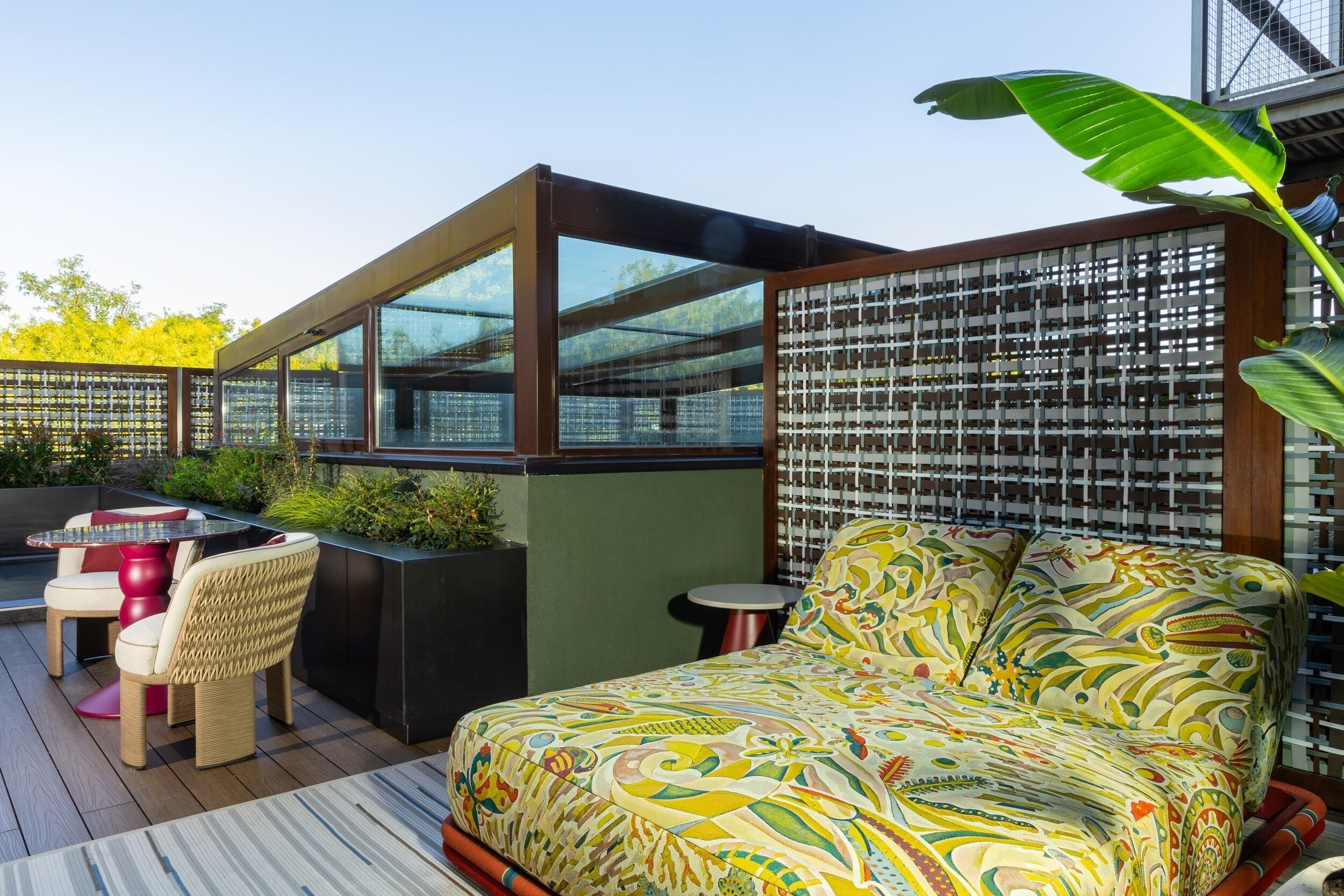 Un área de estar exterior moderna con un sofá y sillas, un cojín estampado y un separador de vidrio.
