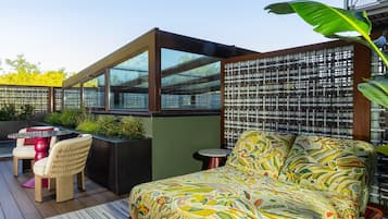 Un área de estar exterior moderna con un sofá y sillas, un cojín estampado y un separador de vidrio.