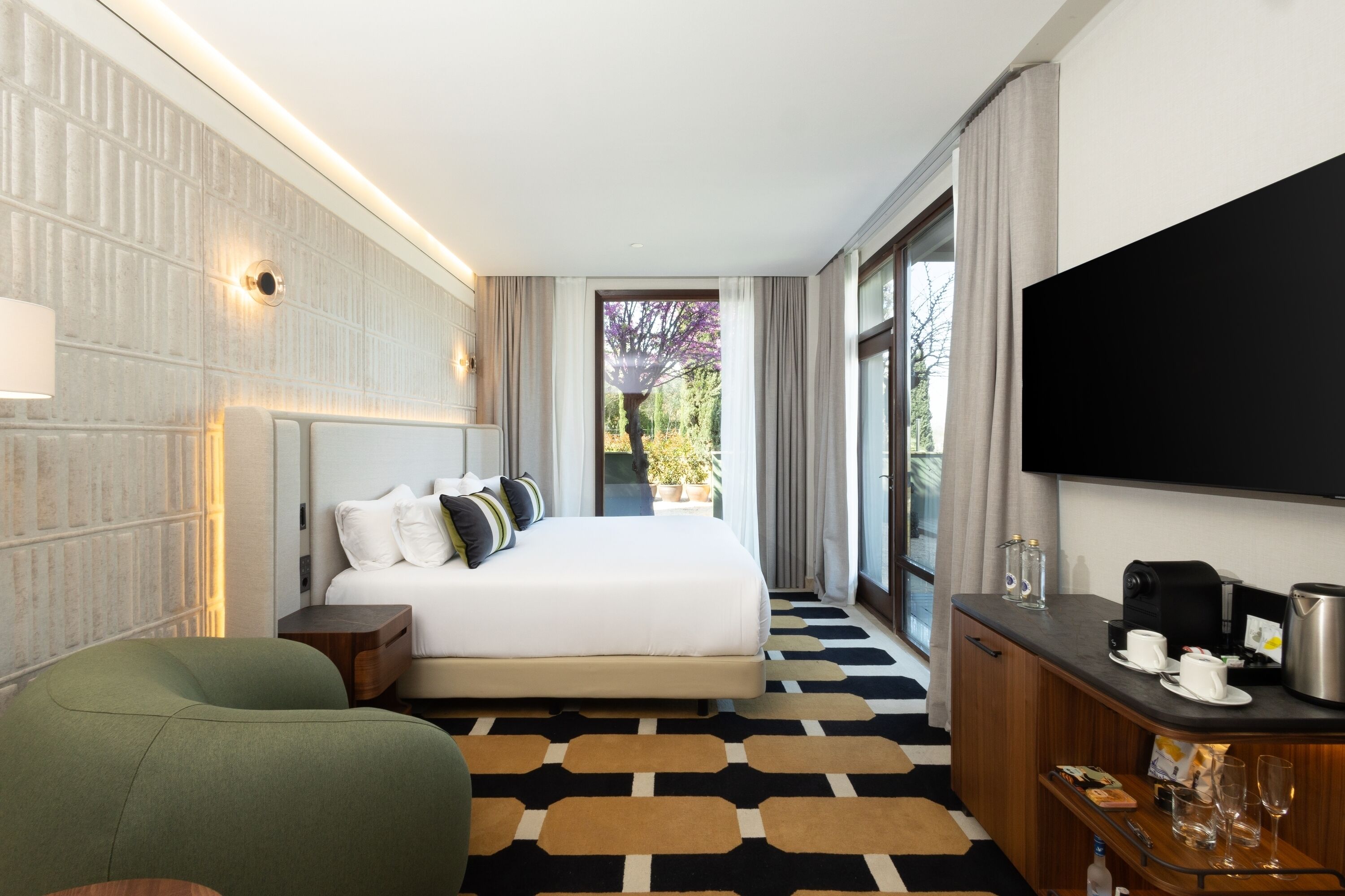 Ein Hotelzimmer mit einem großen Bett, einem Fernseher, einer Kaffeemaschine und Blick auf Bäume durch das Fenster.