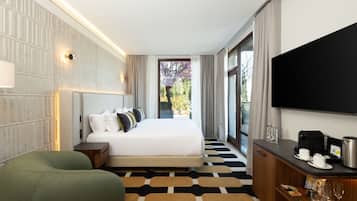 Ein Hotelzimmer mit einem großen Bett, einem Fernseher, einer Kaffeemaschine und Blick auf Bäume durch das Fenster.