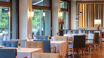 Un restaurante con mesas y sillas, ventanas amplias y paneles decorativos en las paredes.