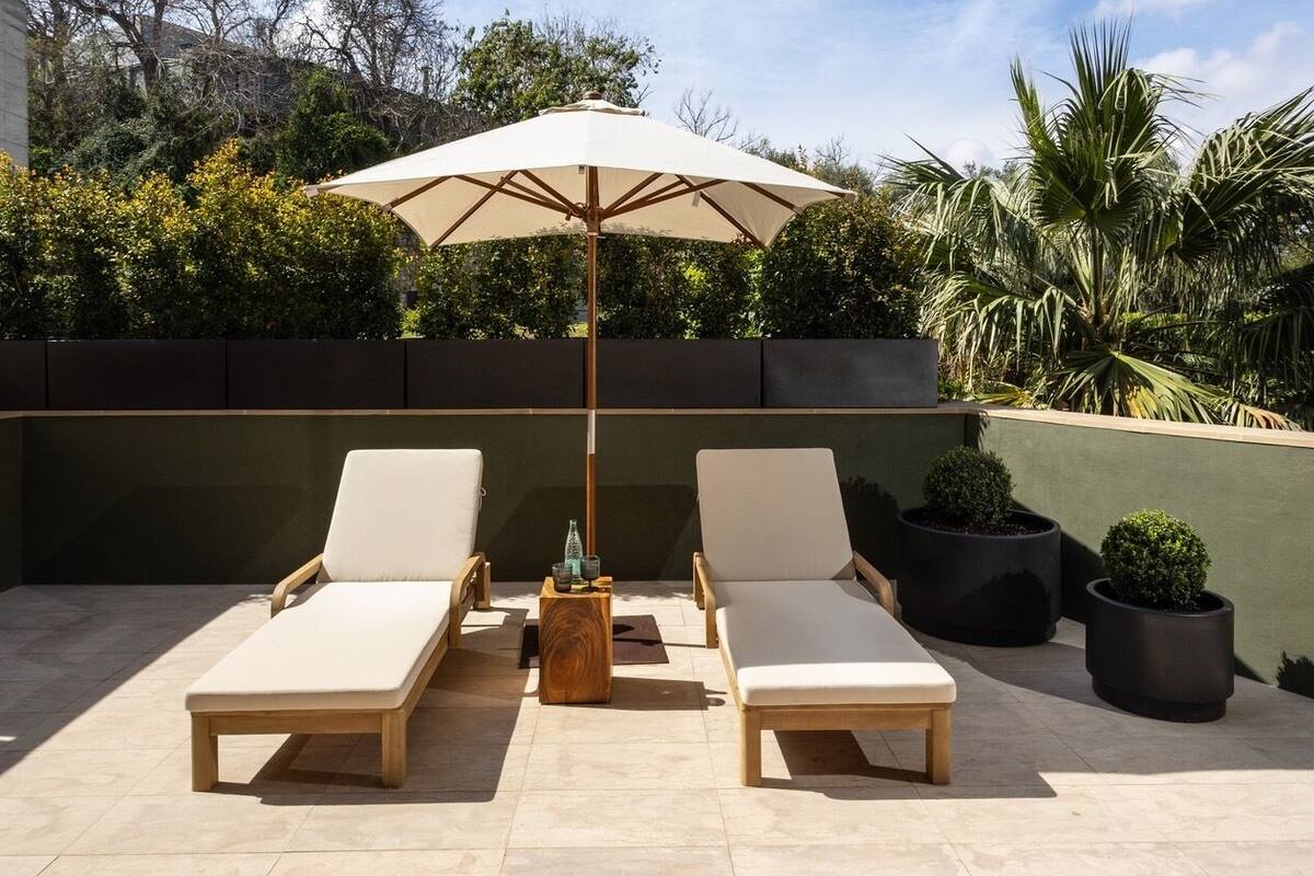 Eine Dachterrasse mit zwei Liegestühlen, einem Holztisch und einem beigen Sonnenschirm.