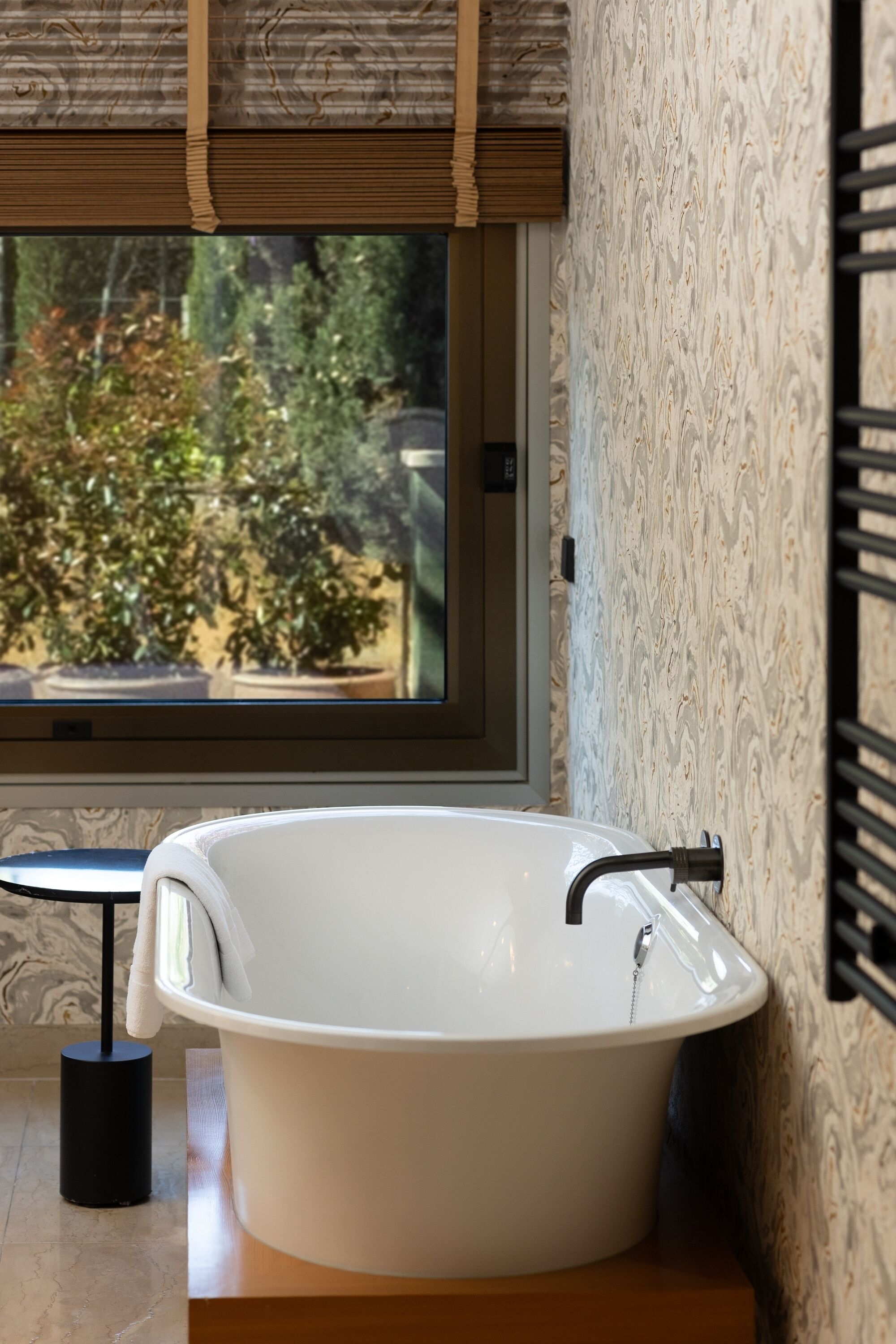 Un baño moderno con una bañera independiente, una ventana con persianas y vistas al exterior.