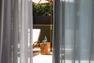 A room with a bed, a wooden side table, and a view of greenery outside.