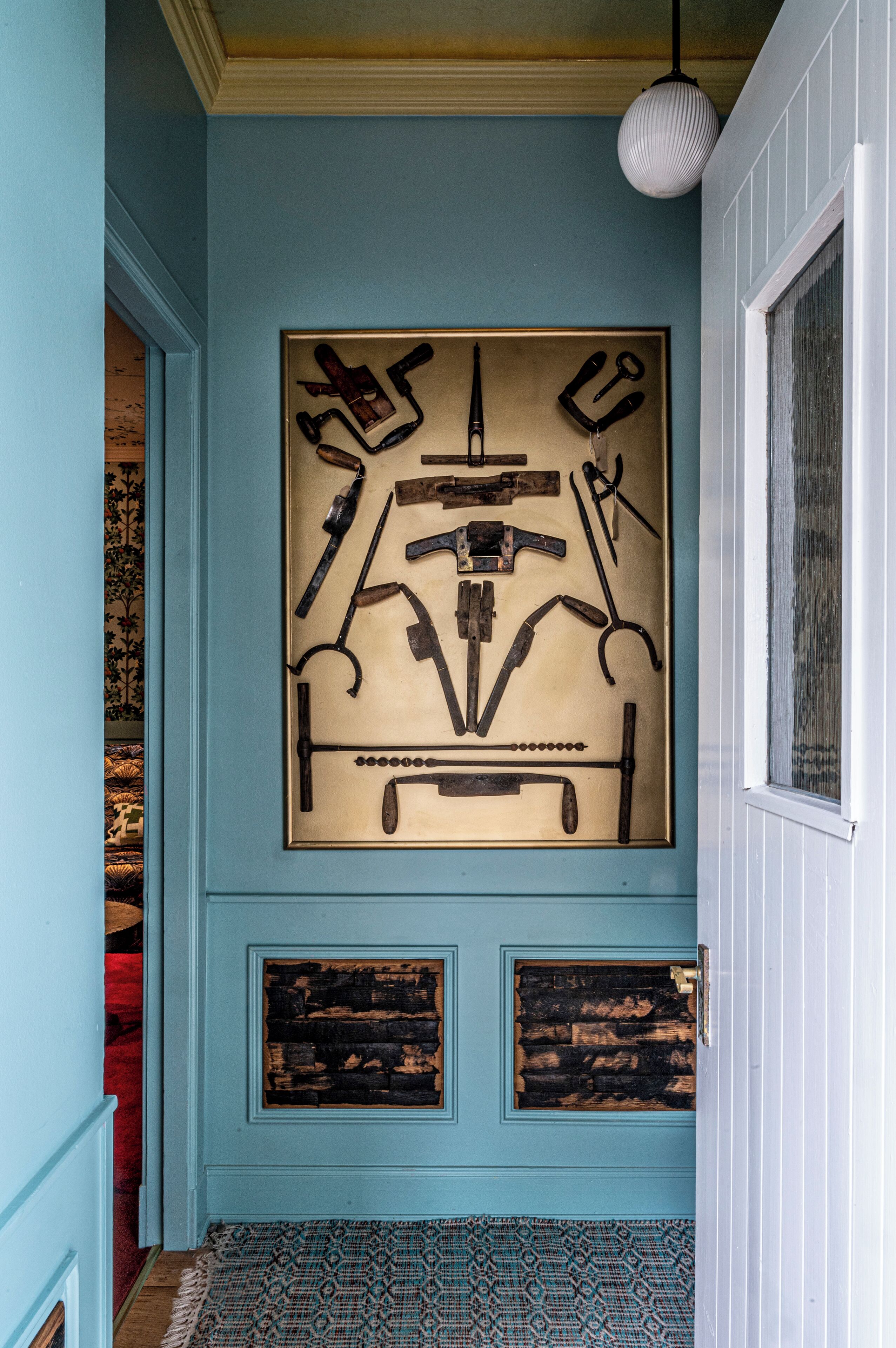 Corredor com porta azul, quadro de ferramentas e tapete estampado.