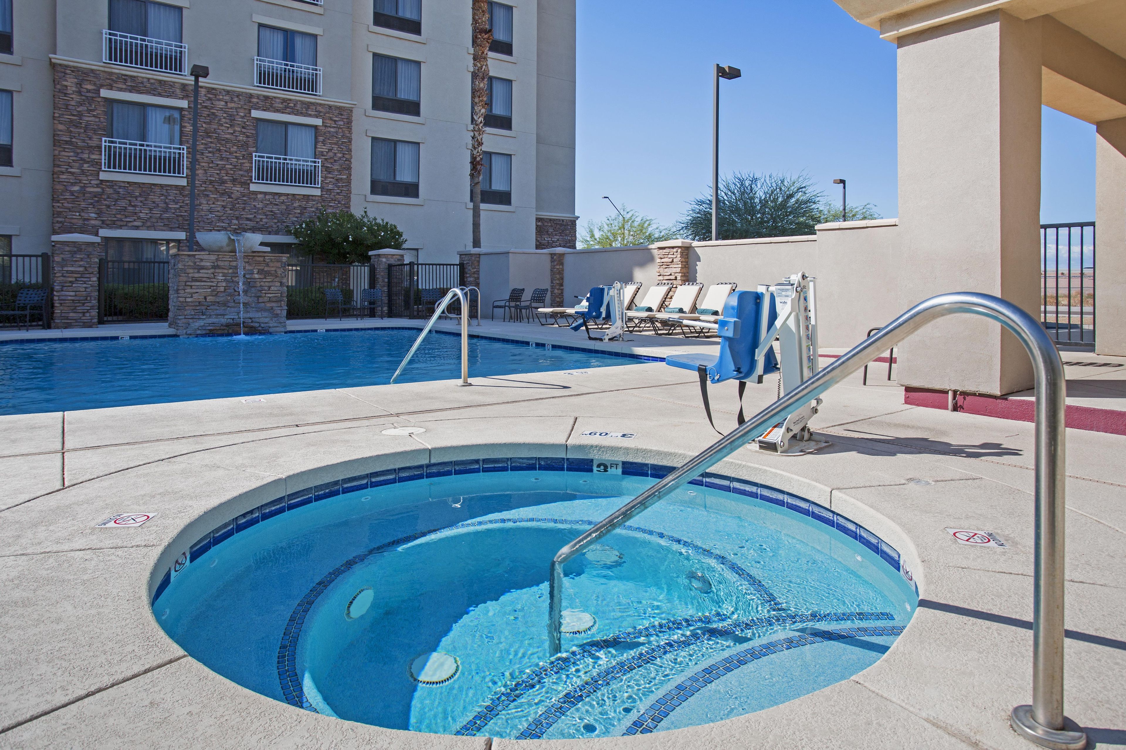 A hotel pool area with a hot tub, lounge chairs, and a stone facade building in the background.
