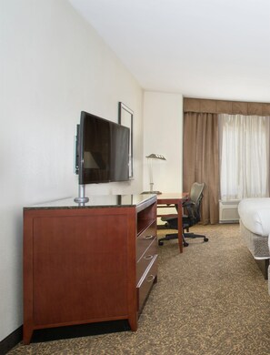 A hotel room with a wooden desk, a television, a chair, a bed, and a window with curtains. - Hilton Garden Inn Avondale (Avondale)
