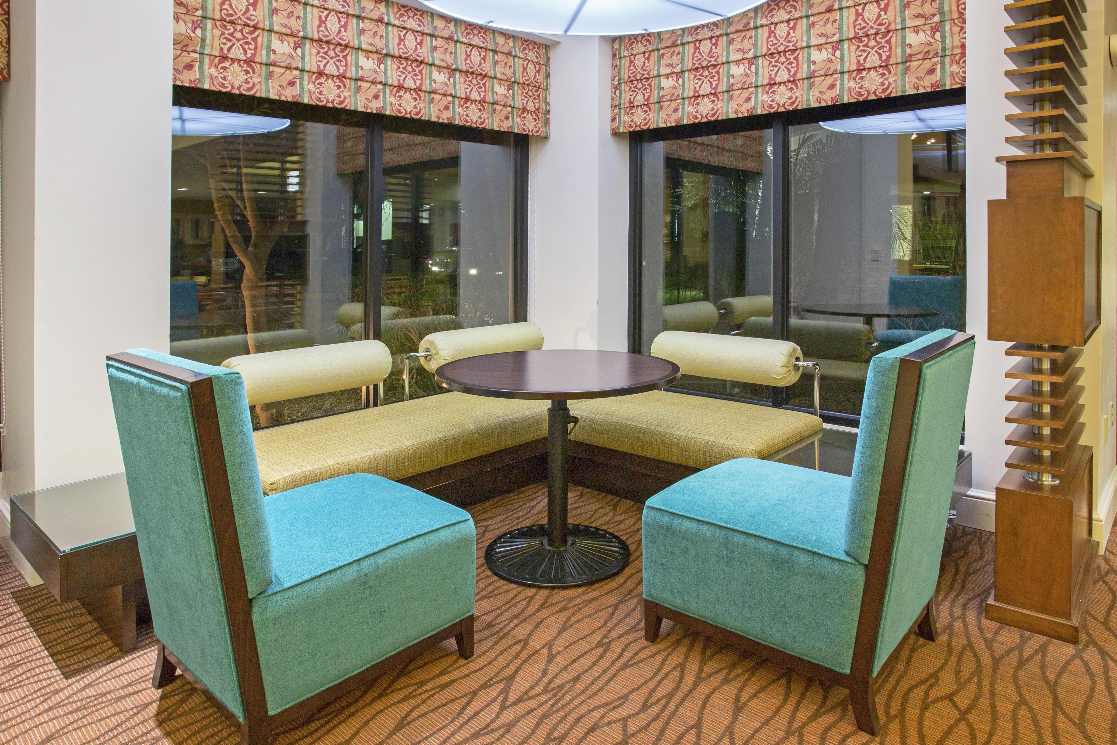 A corner seating area with a round table and four chairs, large windows with patterned curtains, and a wooden column.