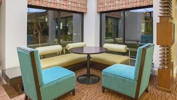 A corner seating area with a round table and four chairs, large windows with patterned curtains, and a wooden column.