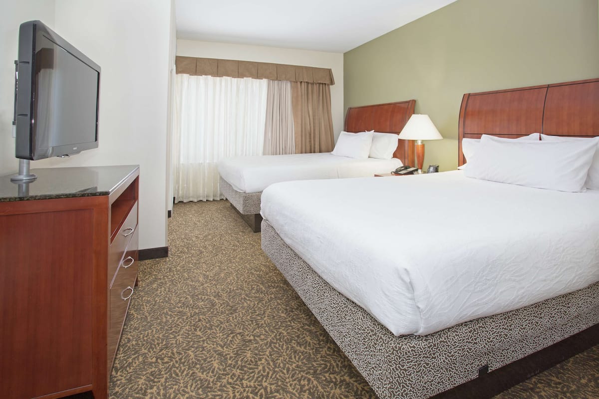 A hotel room with two beds, a TV, a desk, and a lamp.