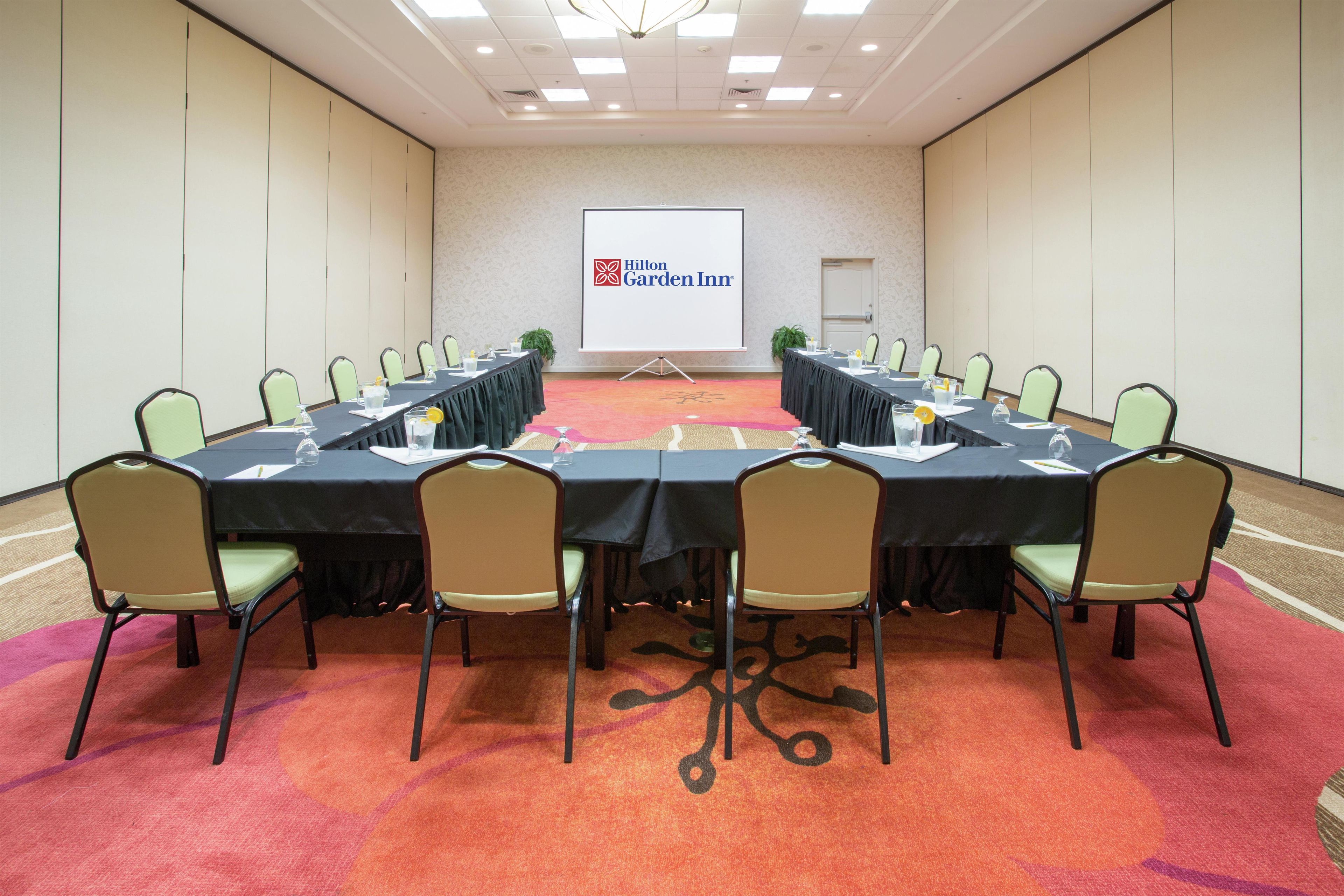 A conference room with a long table, chairs, a projector screen, and a carpeted floor.