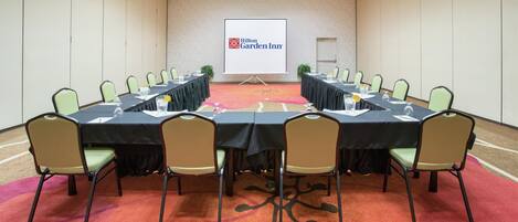 A conference room with a long table, chairs, a projector screen, and a carpeted floor.