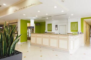A reception area with a counter, a large potted plant, and a green wall.