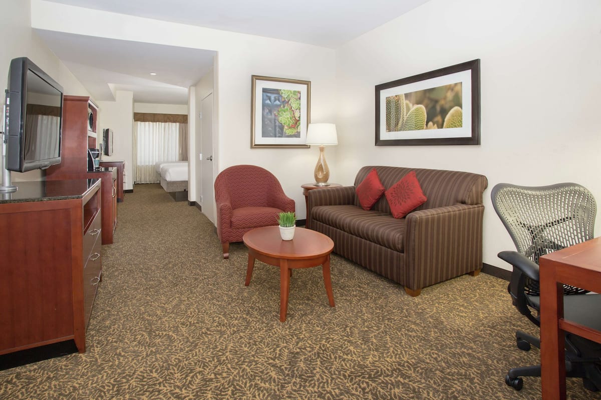 A hotel room with a TV, a sofa, a chair, a small table, and a lamp.