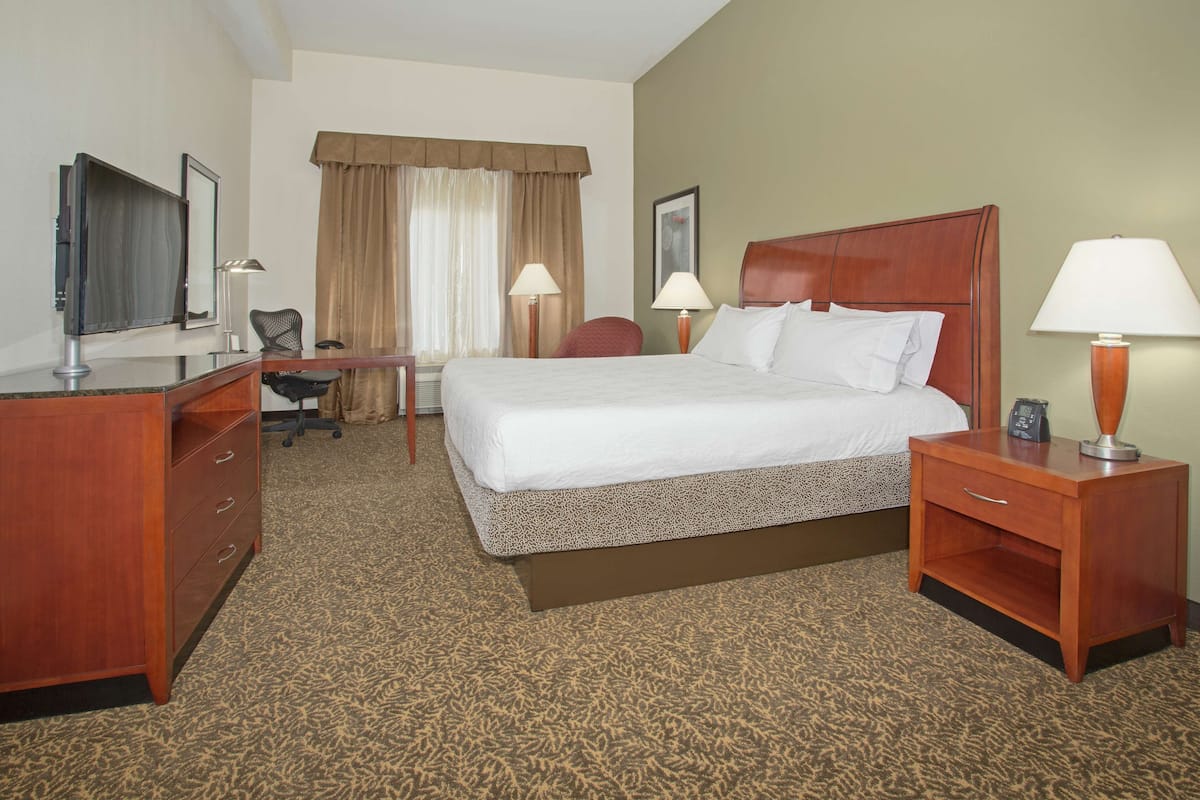 A hotel room with a large bed, a desk, a chair, a TV, and two lamps.