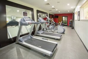 A gym with treadmills, stationary bikes, and a mirrored wall.