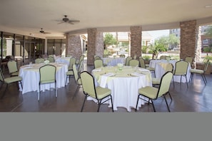 A covered outdoor dining area with round tables and chairs, stone pillars, and a view of buildings and trees. - Hilton Garden Inn Avondale (Avondale)