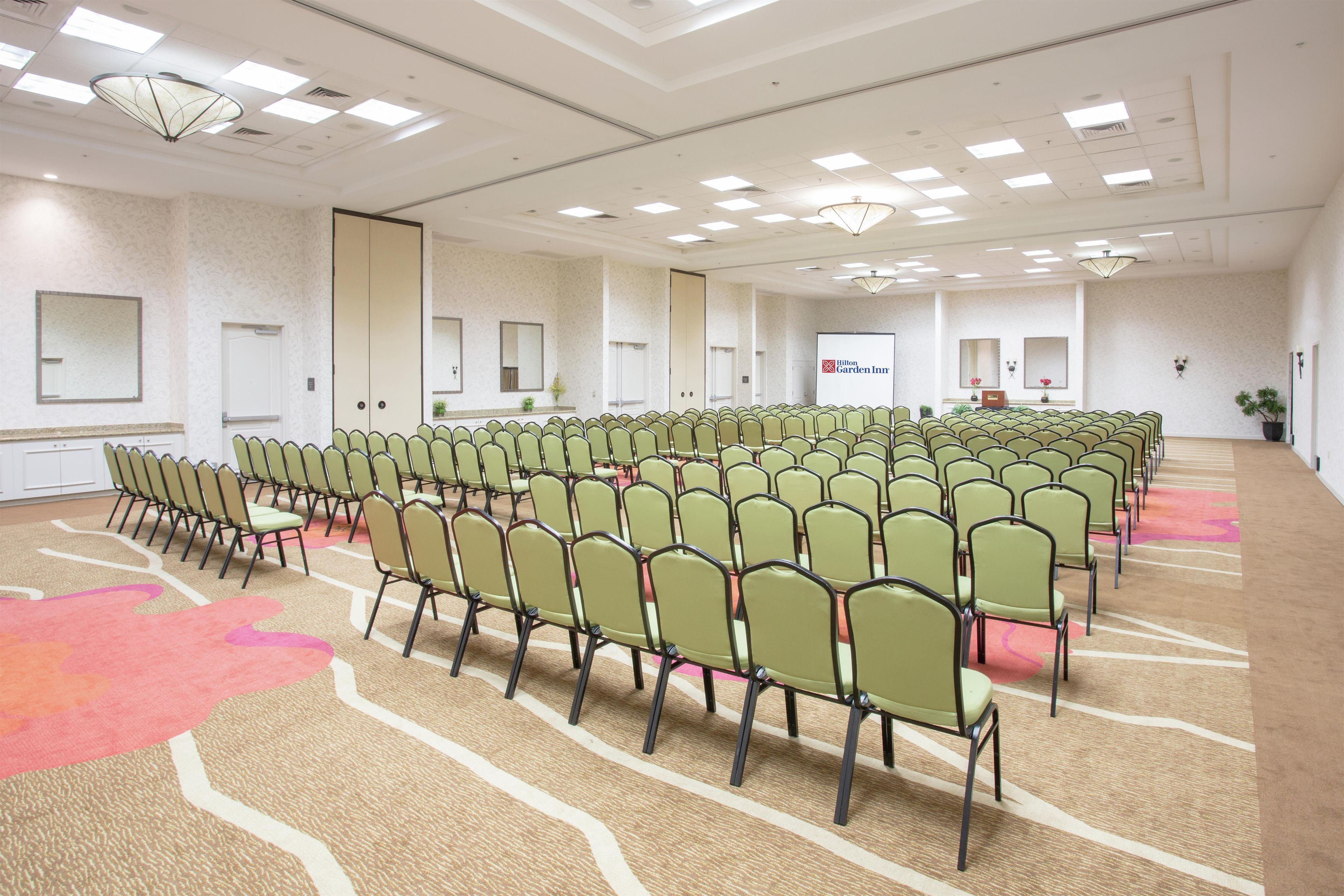 A conference room with rows of chairs, a podium, and a large screen displaying the Hilton Garden Inn logo.
