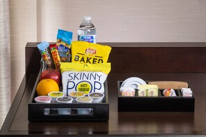 Una bandeja con aperitivos y condimentos, incluyendo papas fritas Lay's Baked, palomitas Skinny Pop sabor cheddar y una botella de agua.