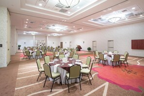 A large conference room with multiple tables and chairs, carpeted flooring, and a high ceiling with recessed lighting.