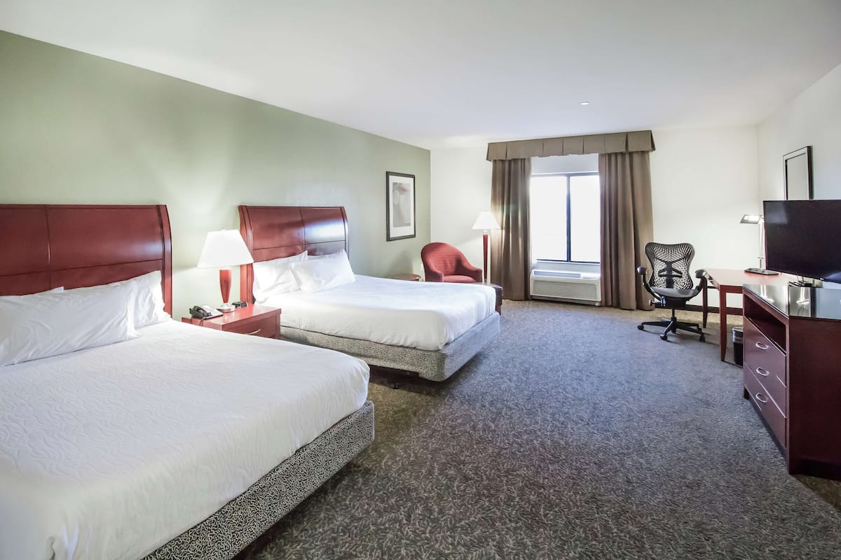 A hotel room with two beds, a desk, a chair, a TV, and a window with curtains.