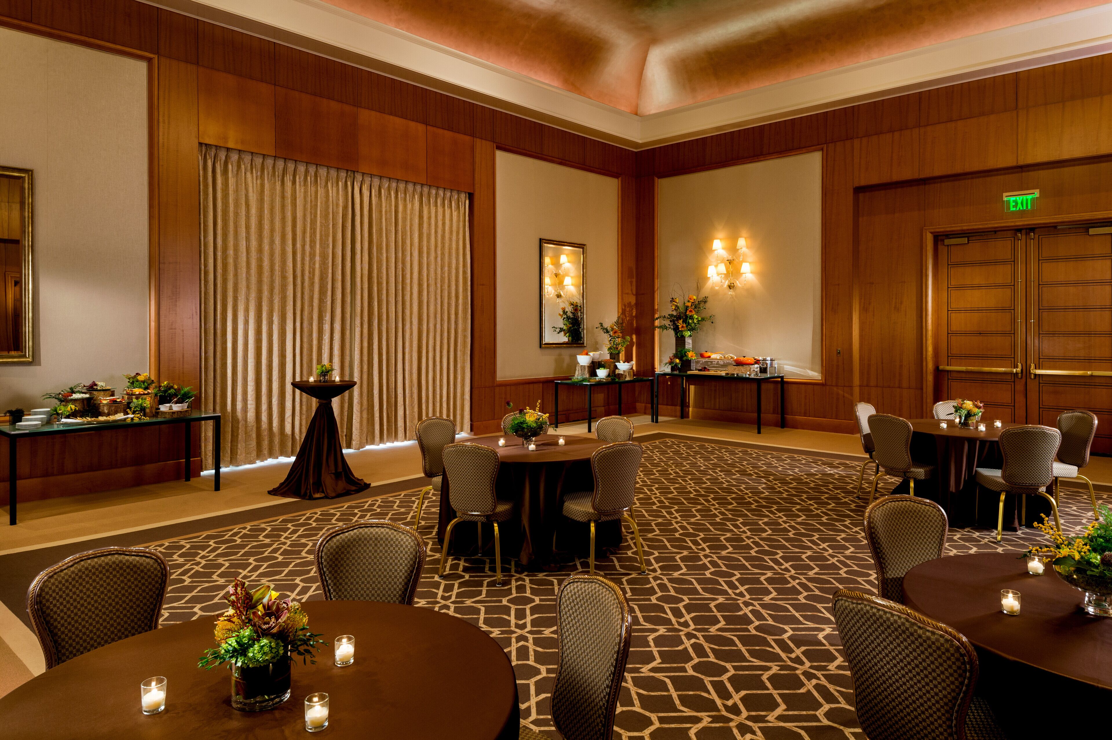A hotel conference room with multiple tables and chairs, a patterned carpet, and a large wooden door.