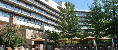 A hotel pool area with sun loungers and umbrellas, surrounded by a multi-story building with balconies.