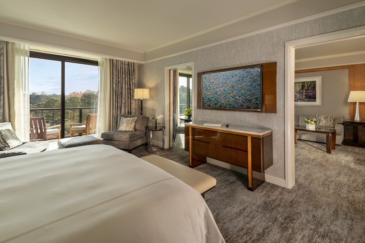 A hotel room with a large bed, a desk, a chair, a balcony with a view, and artwork on the walls.